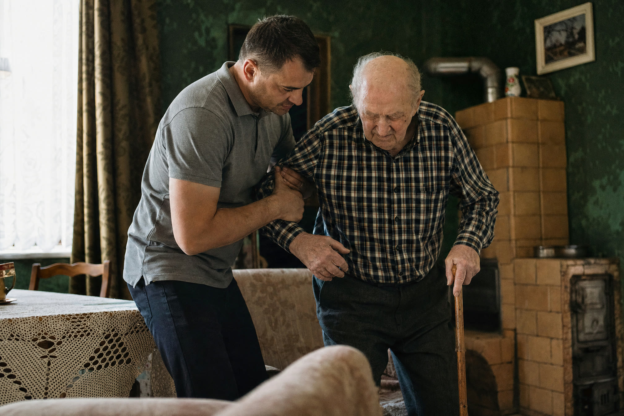 Opiekun pomaga seniorowi wstać z fotela